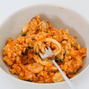 A fork in a white bowl filled with a risotto made with seafood