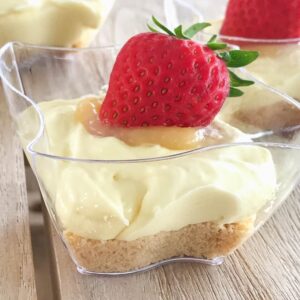 An individual lemon cheesecake in a glass bowl with a fresh strawberry on top