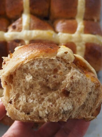 side view of adult holding hot cross bun.