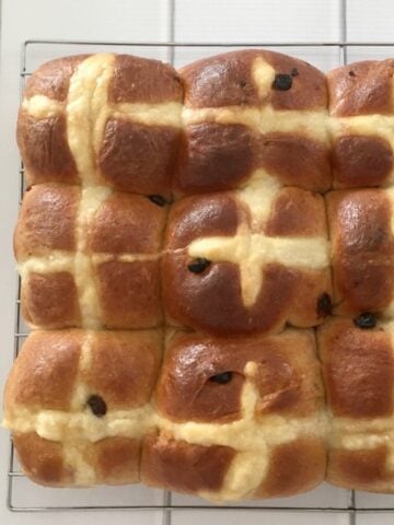 A batch of fruity Hot Cross Buns baked together and resting on a wire rack.