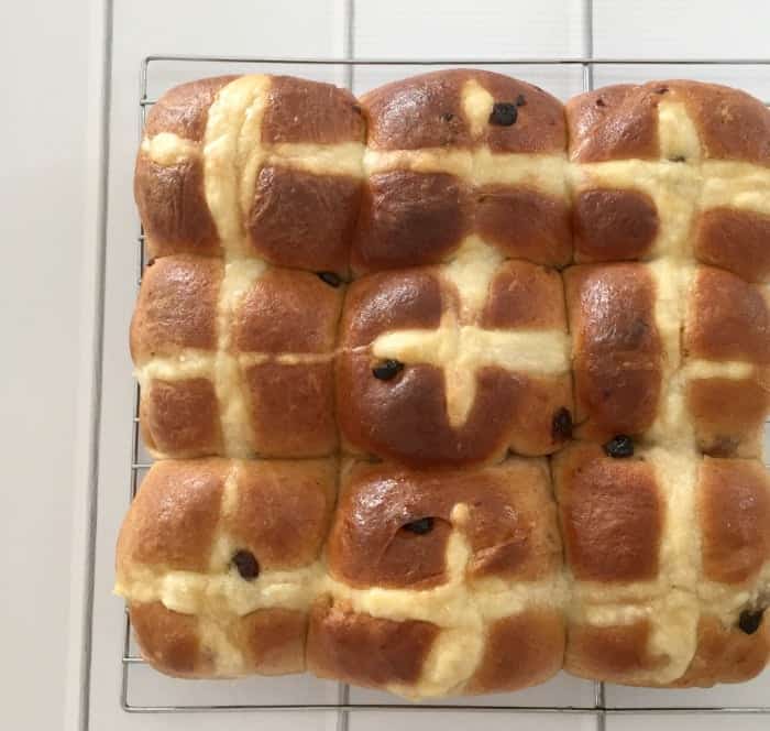 A batch of fruity Hot Cross Buns baked together and resting on a wire rack.