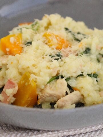 A bowl of risotto with pumpkin, chicken, bacon and spinach.