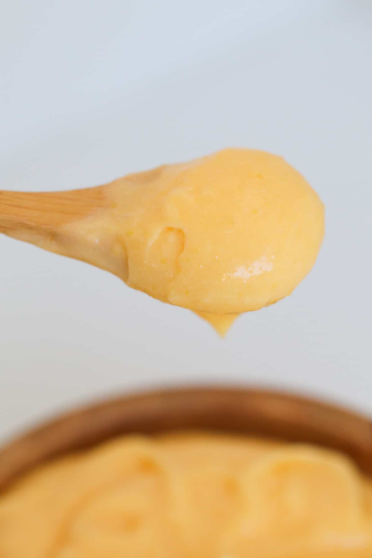 A wooden spoon holding creamy lemon curd.