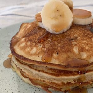 A stack of banana pancakes with sliced banana on top, and drizzled with maple syrup