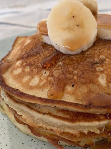 A stack of banana pancakes with sliced banana on top, and drizzled with maple syrup