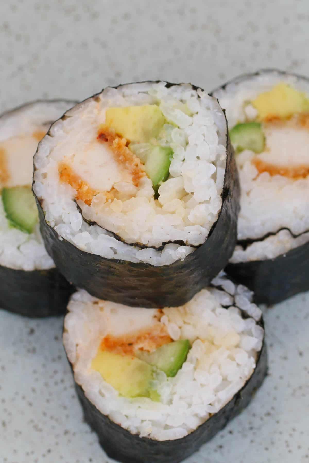 A stack of sushi with chicken and avocado on a plate.
