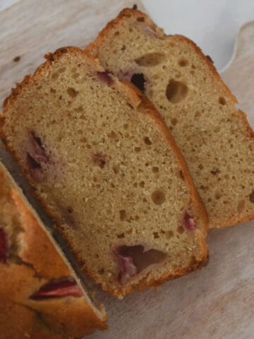 A banana and strawberry loaf with two slices cut showing strawberries baked inside.