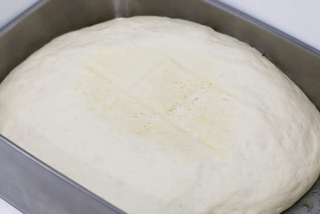 Pizza dough that has been proved in a stainless steel container.