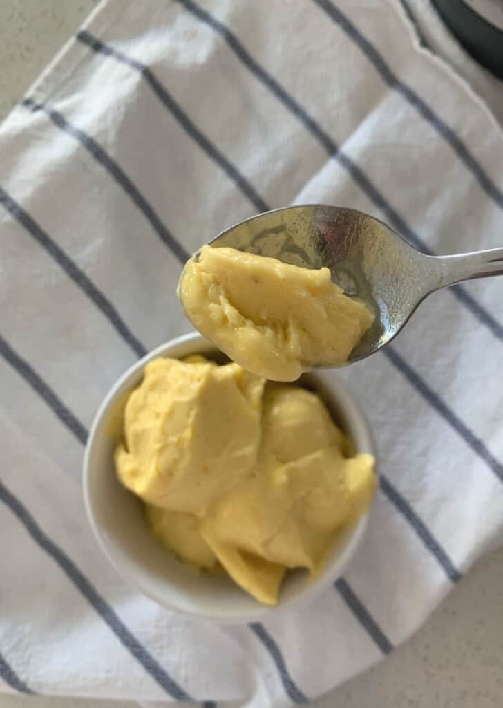 Mango ice cream in a bowl with a spoon on top of a striped tea towel 