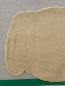 Pizza dough rolled out flat on bench