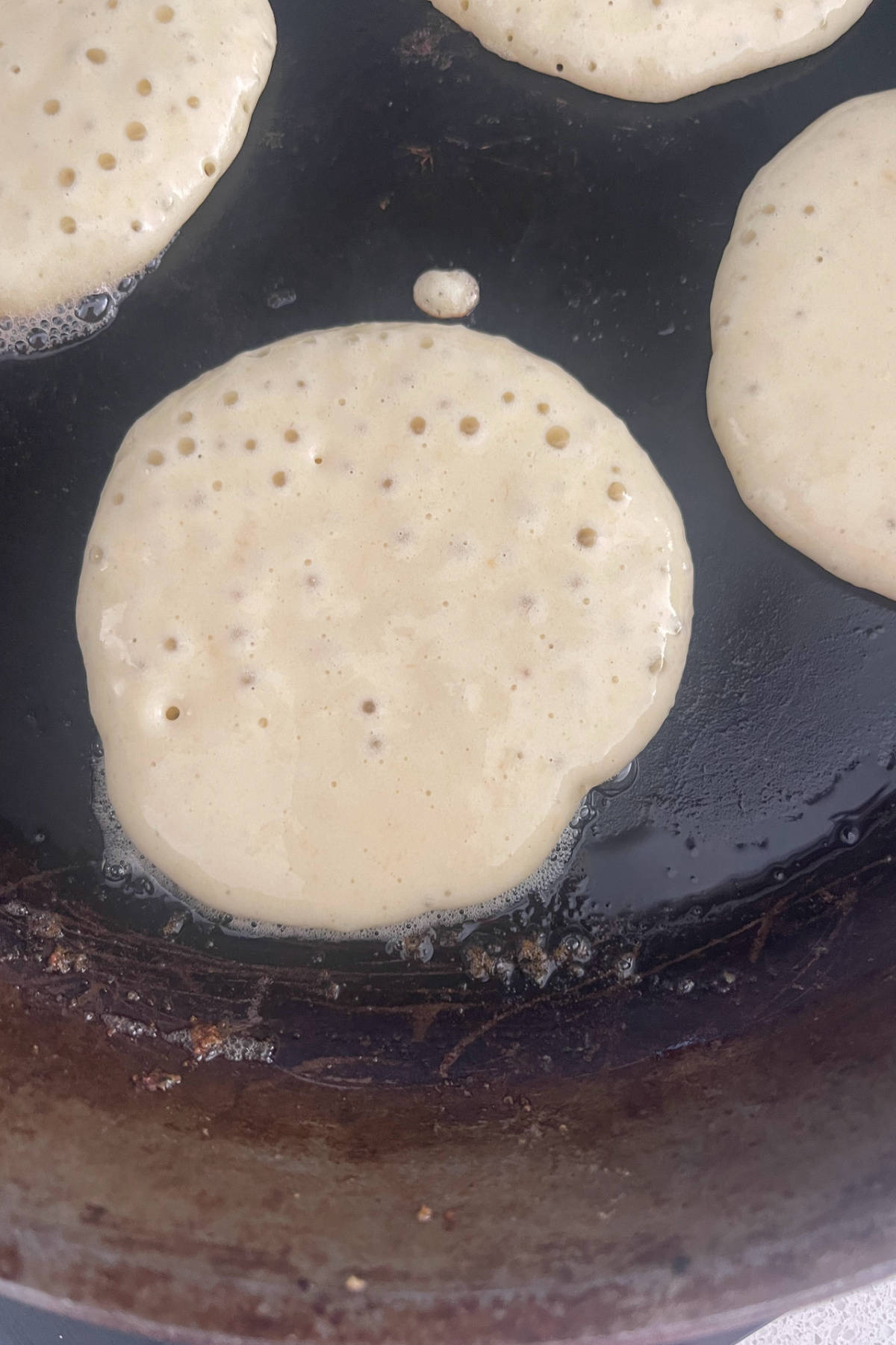 Banana pikelet in a frying pan with bubbles on one side.
