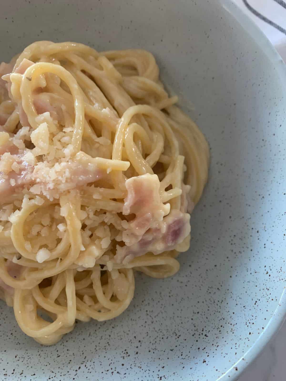 Top close up view of carbonara in a green bowl with parmesan on top