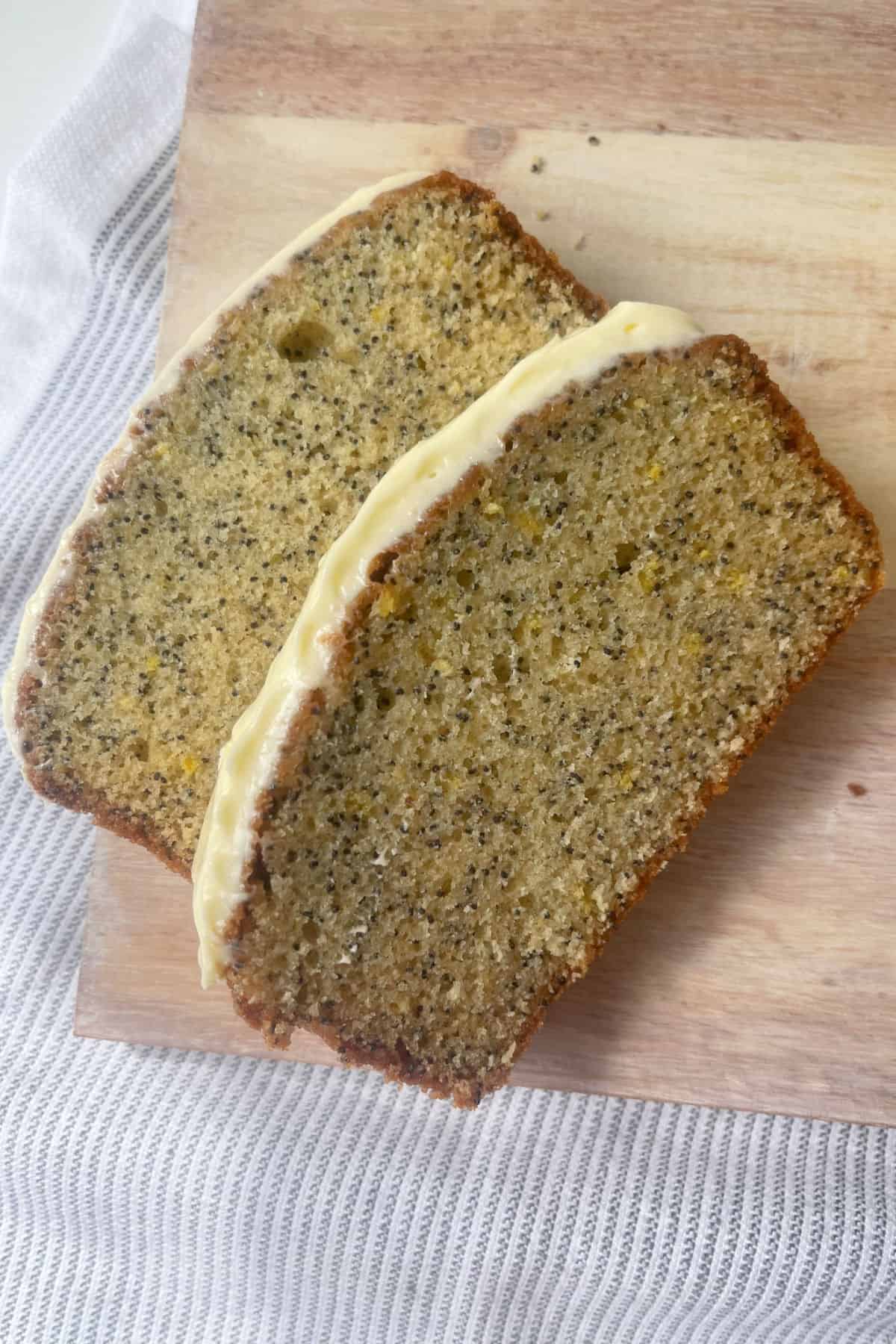 Overhead view of Lemon and Poppy Seed Cake Sliced and sitting on a pale timber serving board.
