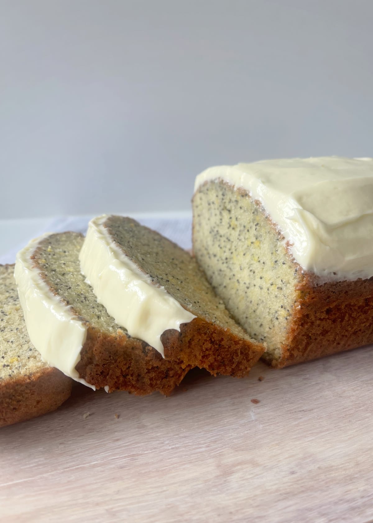 Lemon and Poppy Seed Cake Sliced and sitting on a pale timber serving board.