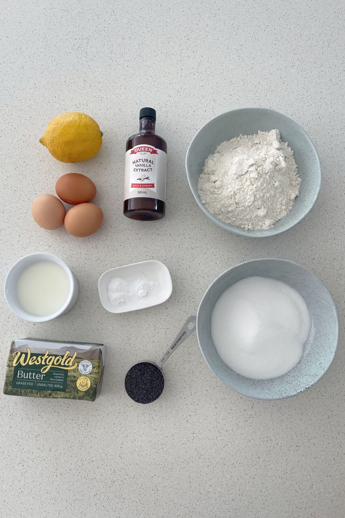 Ingredients to make a Lemon and Poppy Seed cake on a speckled bench.