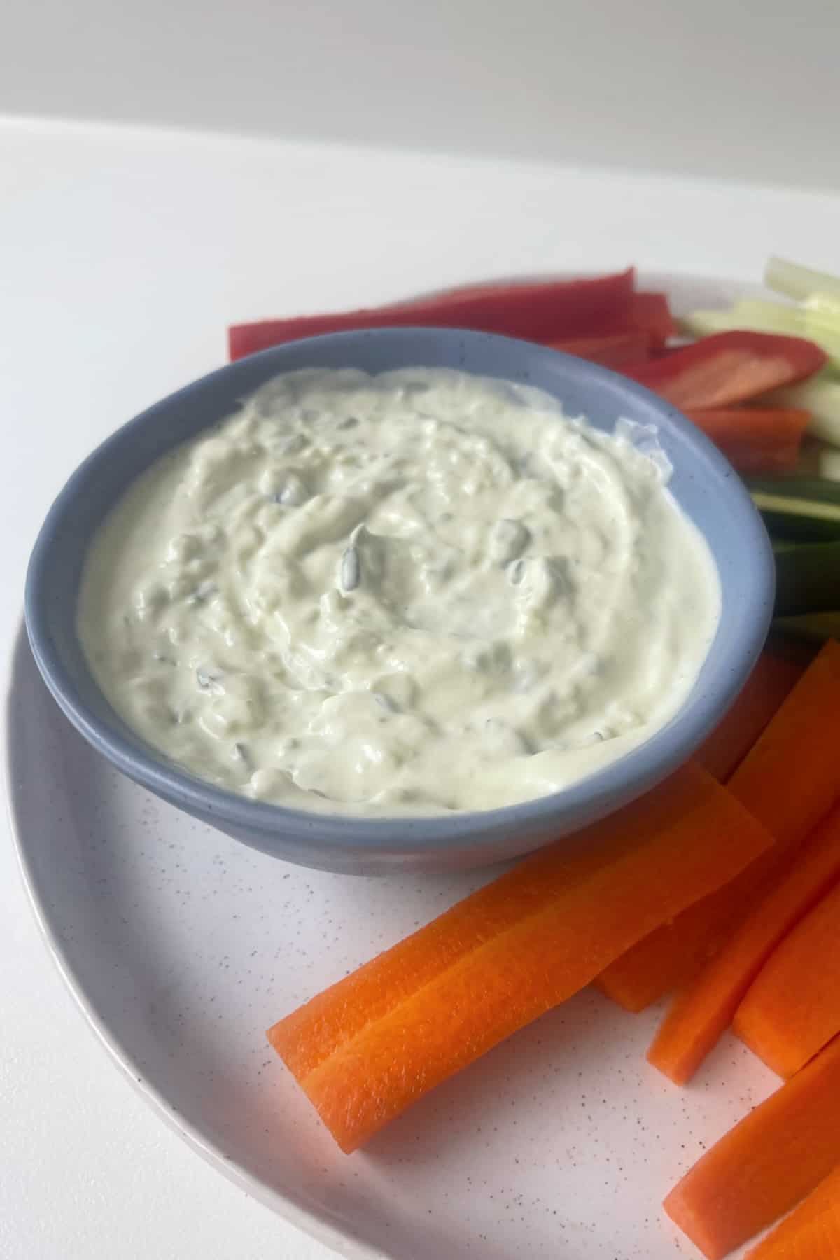 Side view of Tzatziki Dip in a blue serving bowl surrounded by veggie sticks.