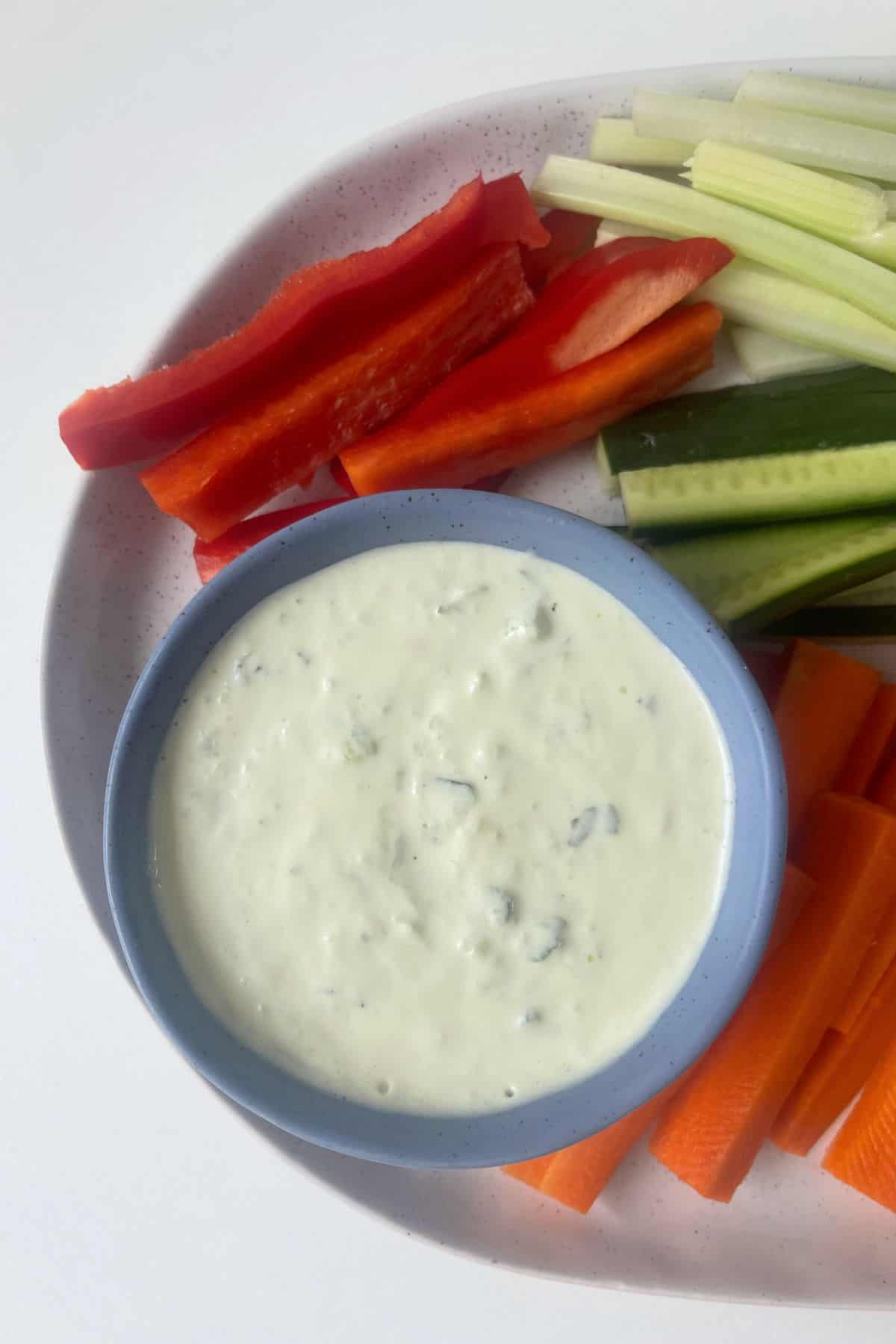 Overhead view of Tzatziki Dip in a blue serving bowl surrounded by veggie sticks.