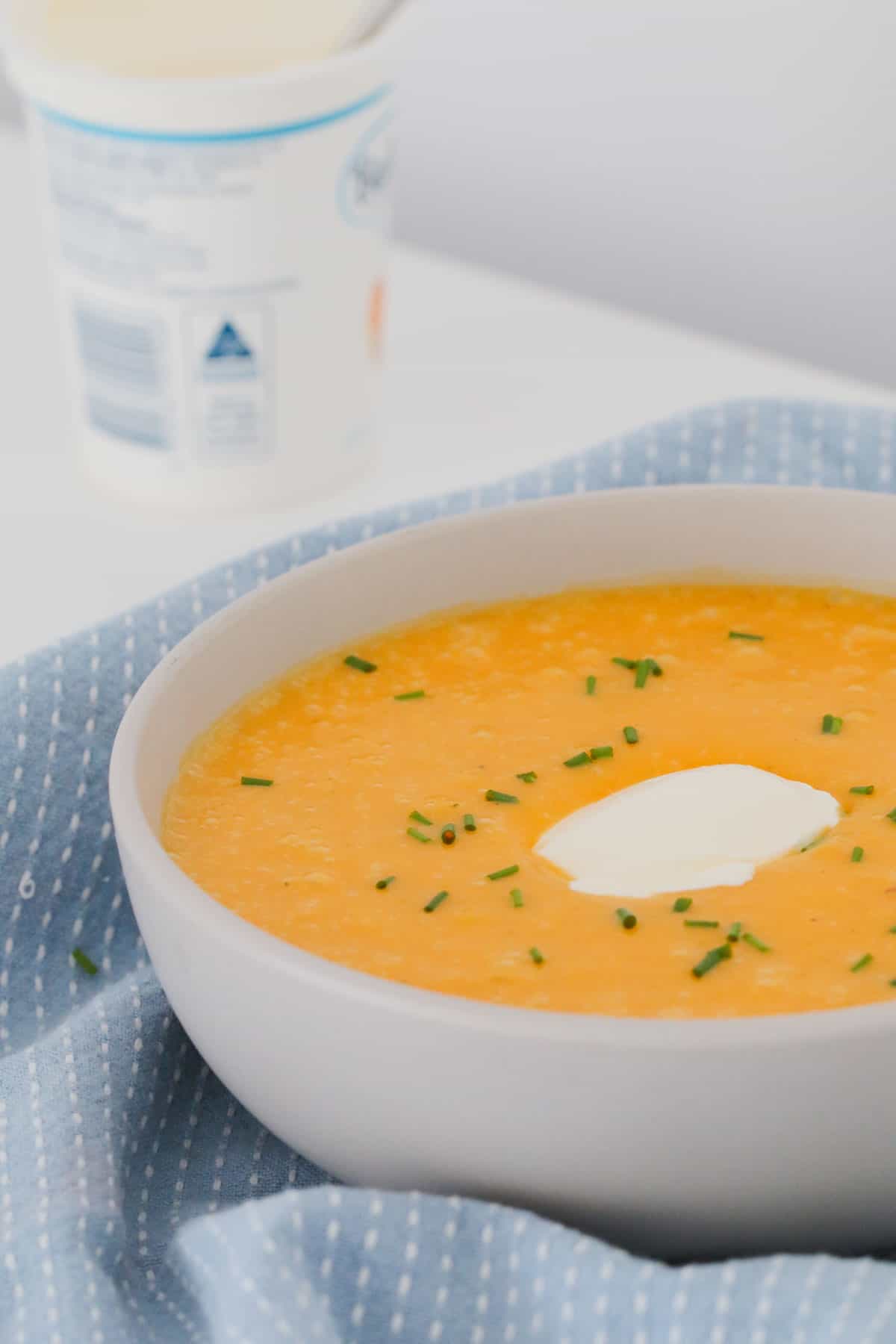 Sour cream and chives on top of a bowl of pumpkin soup.
