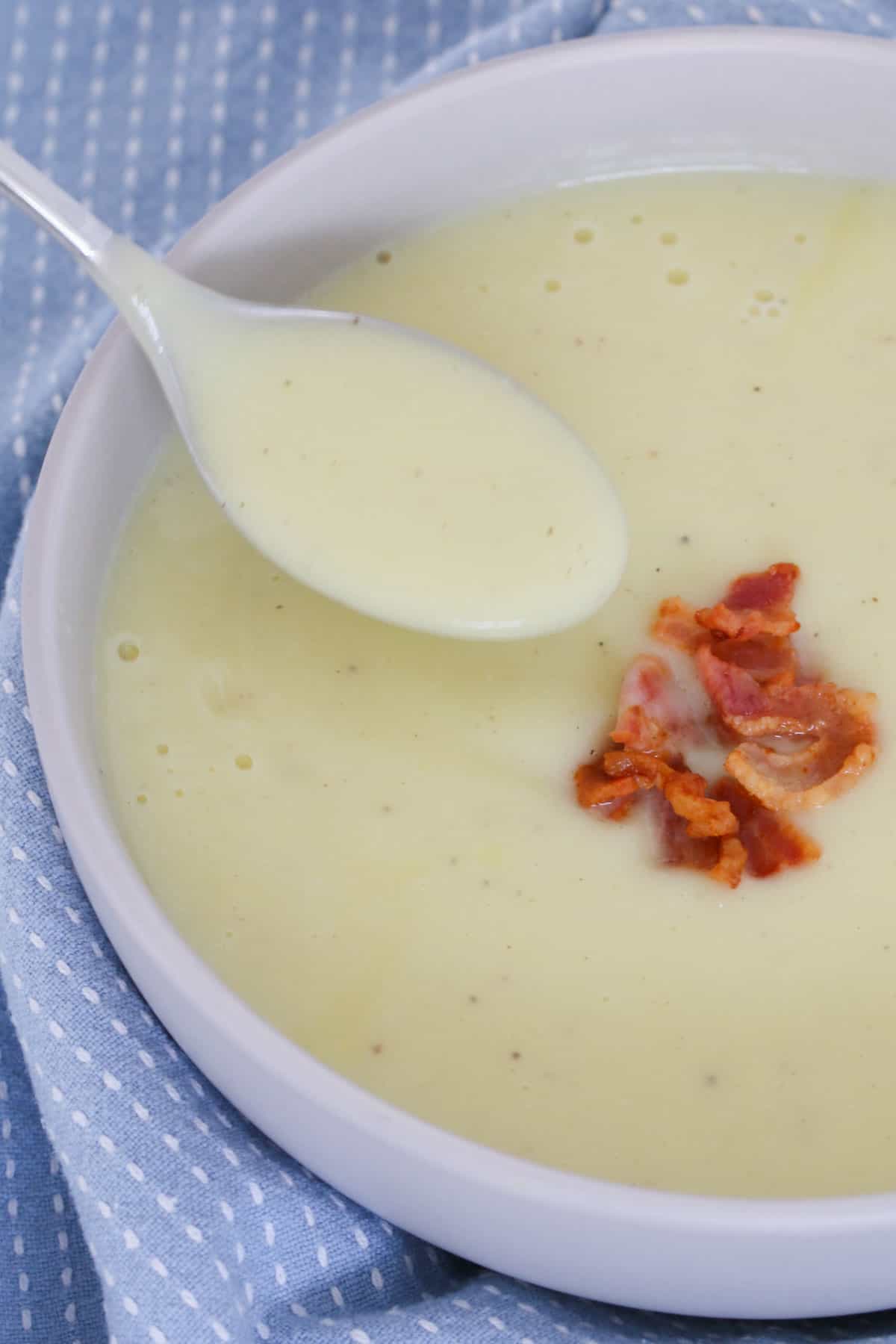 A spoon in a bowl of cauliflower soup with bacon crumbs.