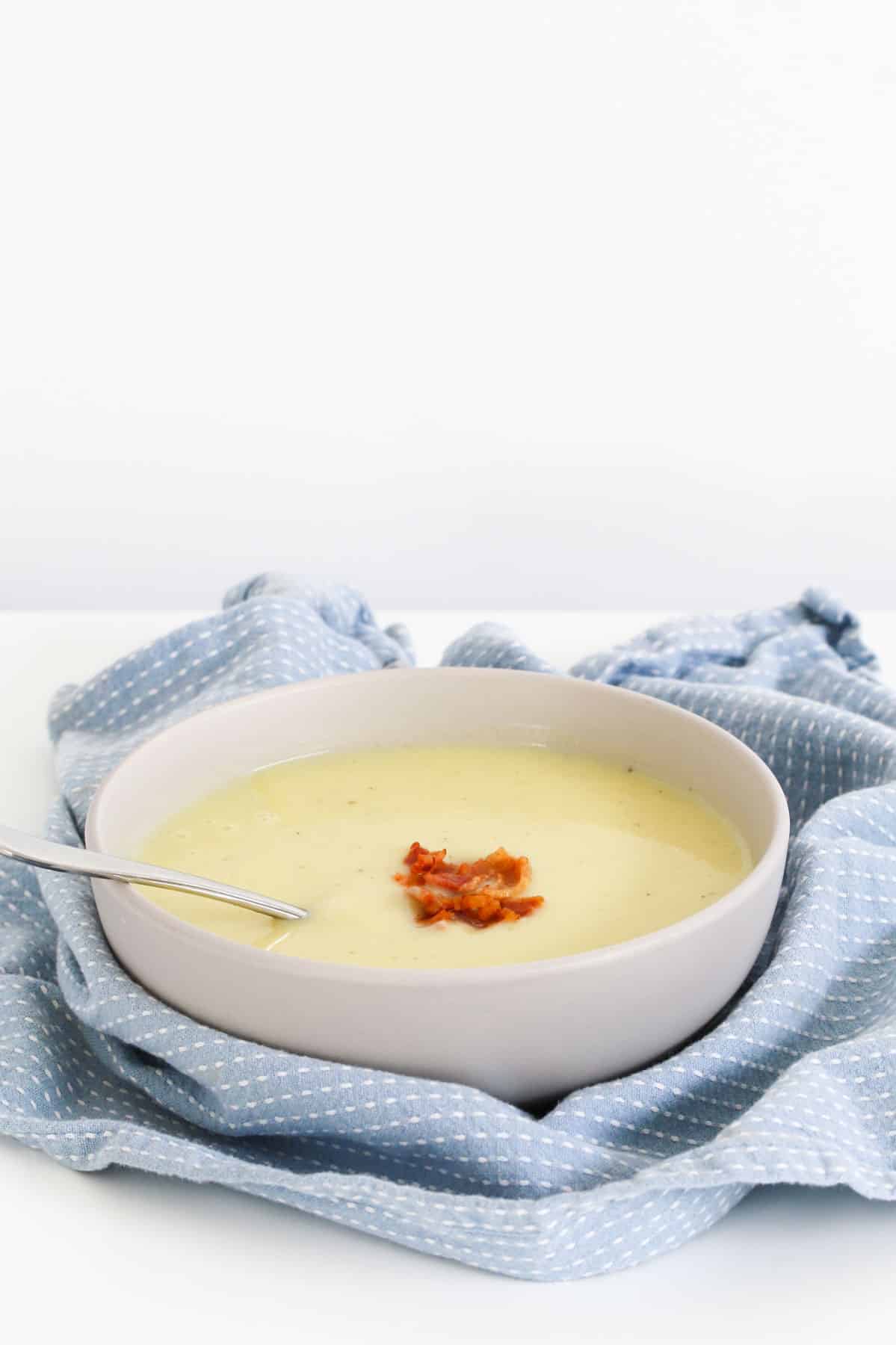 A blue tea towel around a bowl of white soup with bacon.