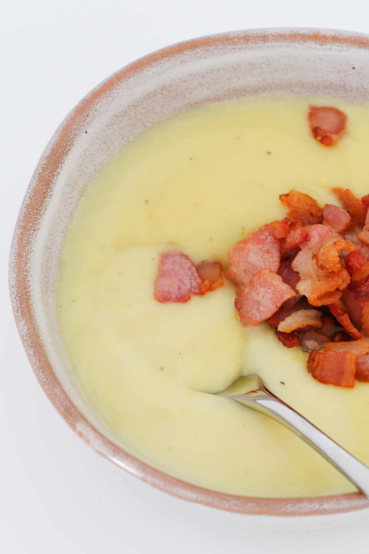 A spoon in a bowl of bacon topped soup.