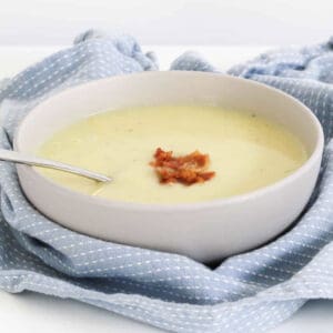 A blue tea towel around a bowl of white soup with bacon.