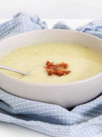 A blue tea towel around a bowl of white soup with bacon.