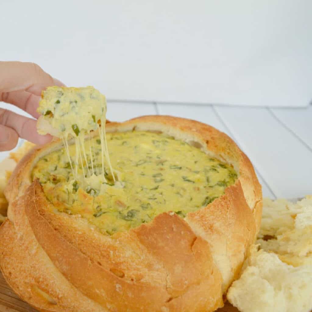 a piece of bread being used to scoop up spinach cob loaf dip