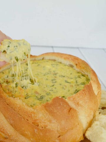a piece of bread being used to scoop up spinach cob loaf dip