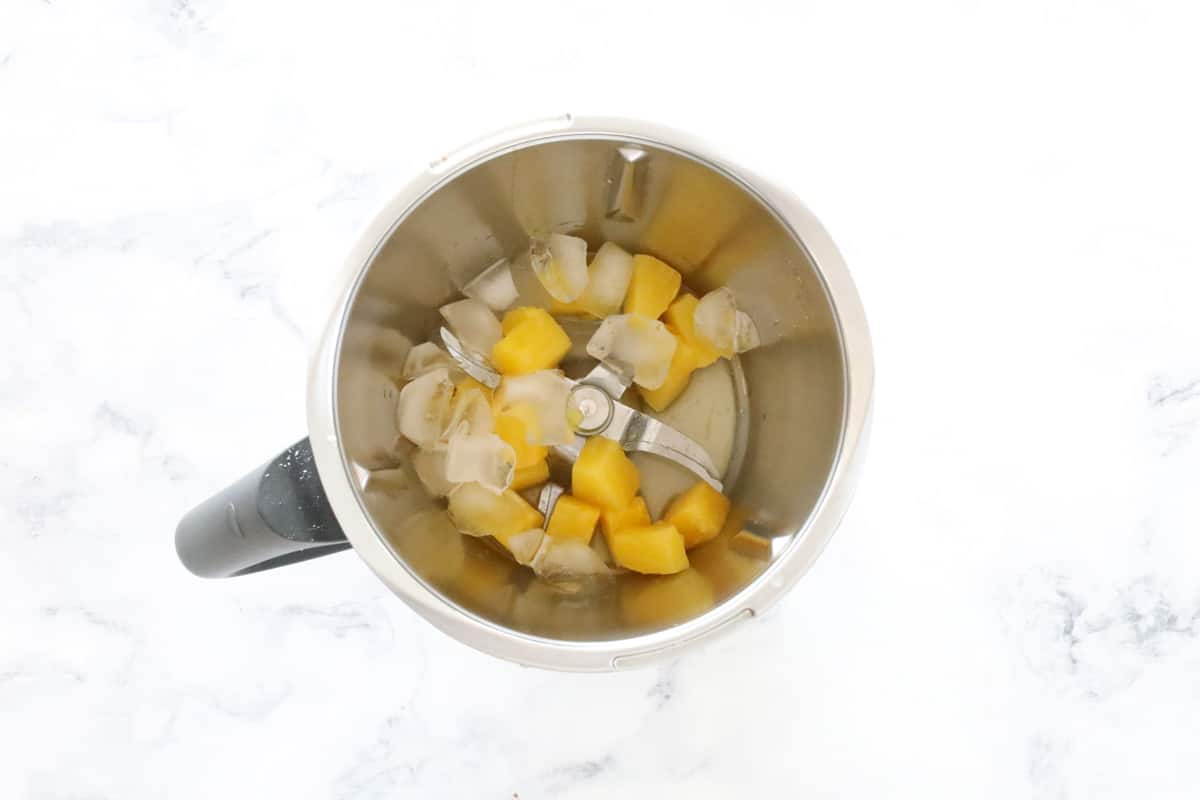 Pineapple and ice in a Thermomix bowl.