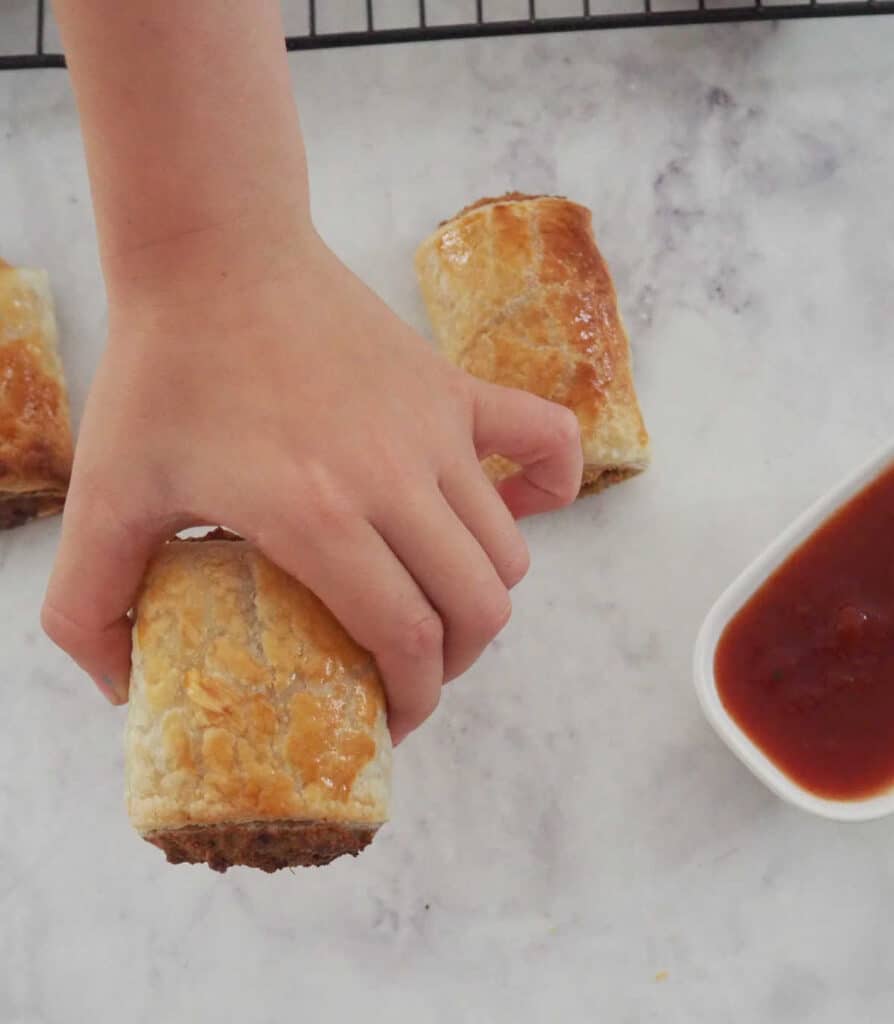 Childs hand reaching for a Vegetarian Sausage Roll.