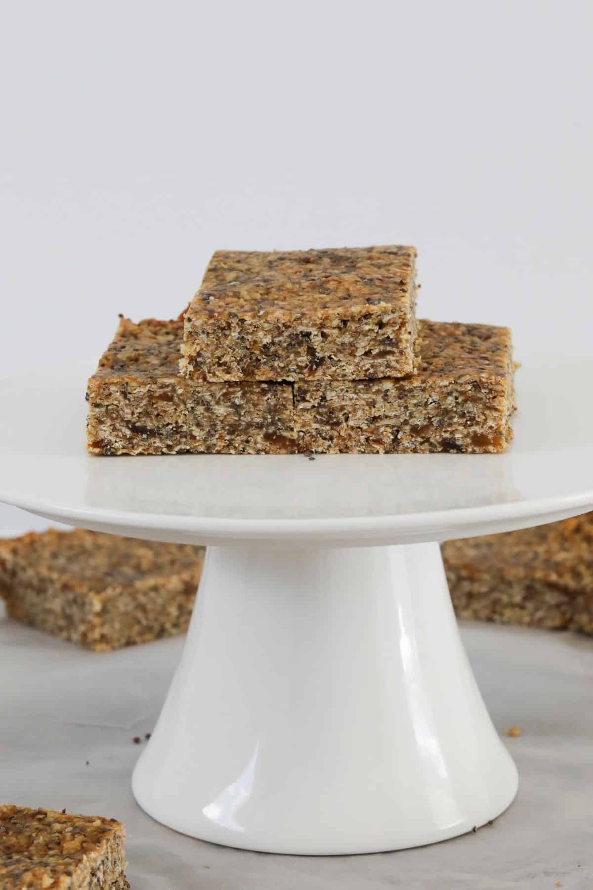 Pieces of homemade and healthy seed muesli bars on a white cake stand.