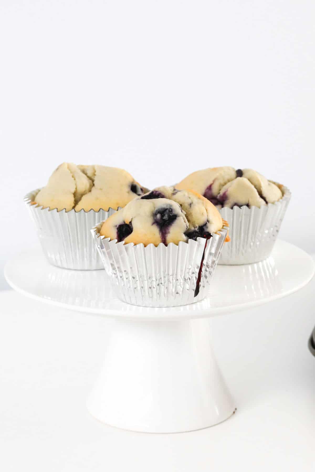 Three muffins with fruit on a cake stand.