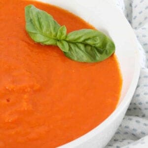A bowl of tomato soup with basil on top.