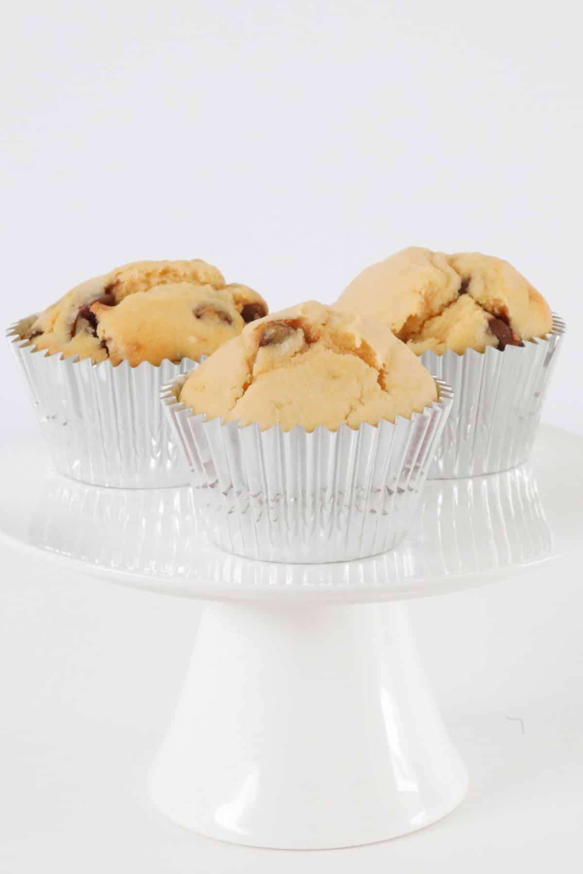Three chocolate chip muffins on a cake stand.
