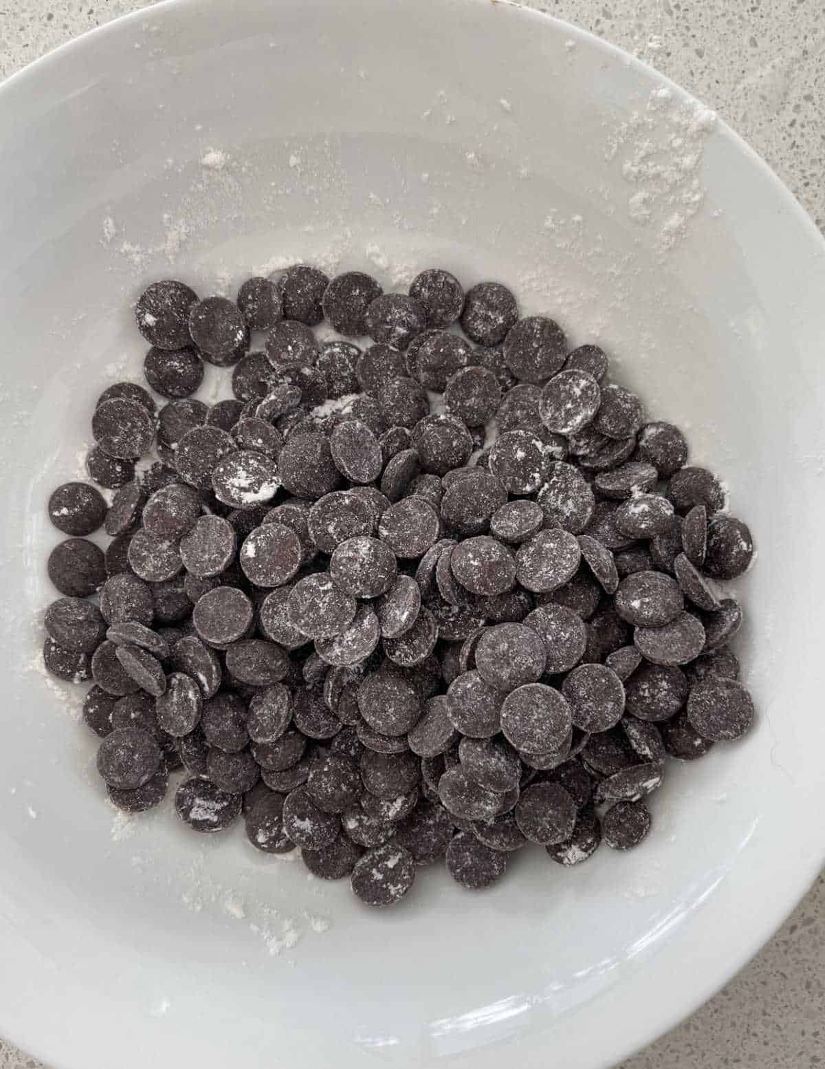 chocolate chips dusted with flour in a white bowl.