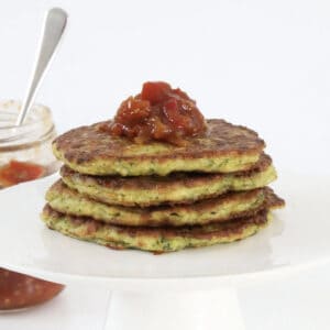 A stack of zucchini fritters with chutney on top.