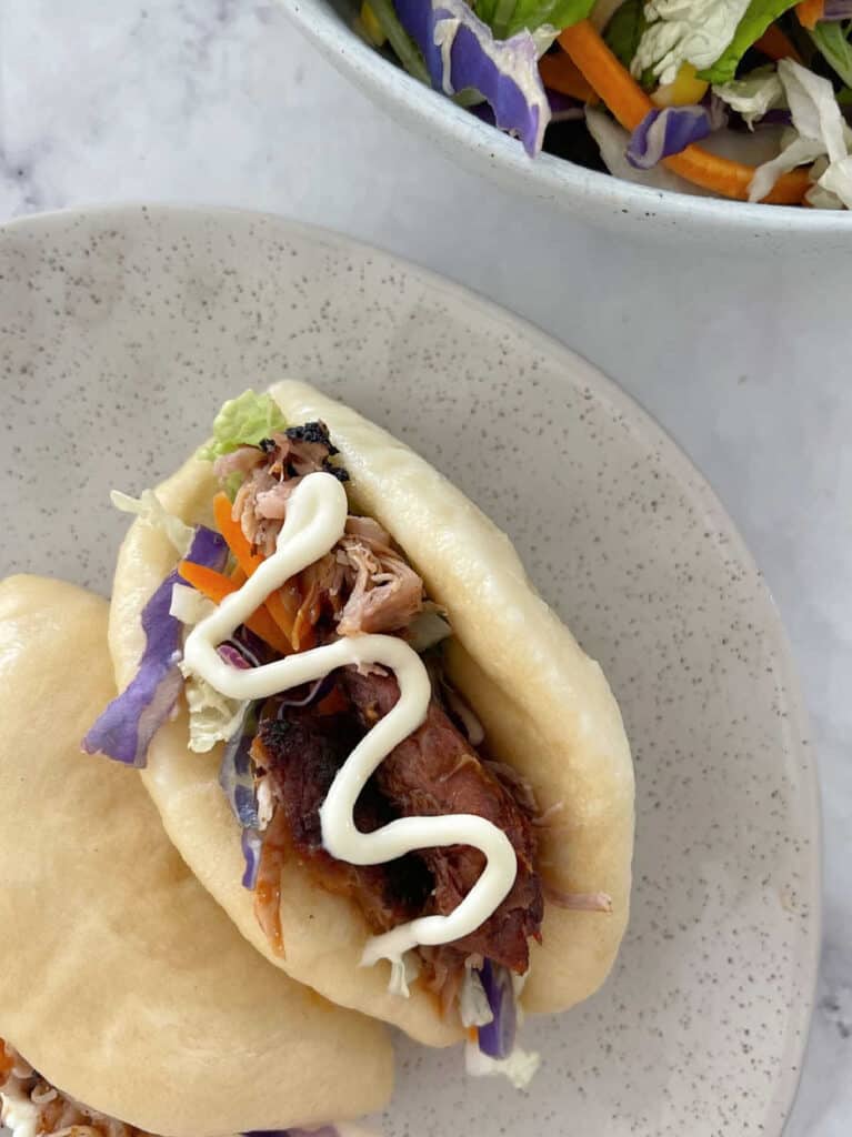 Thermomix Bao Buns filled with salad and roast bbq pork on a speckled plate.