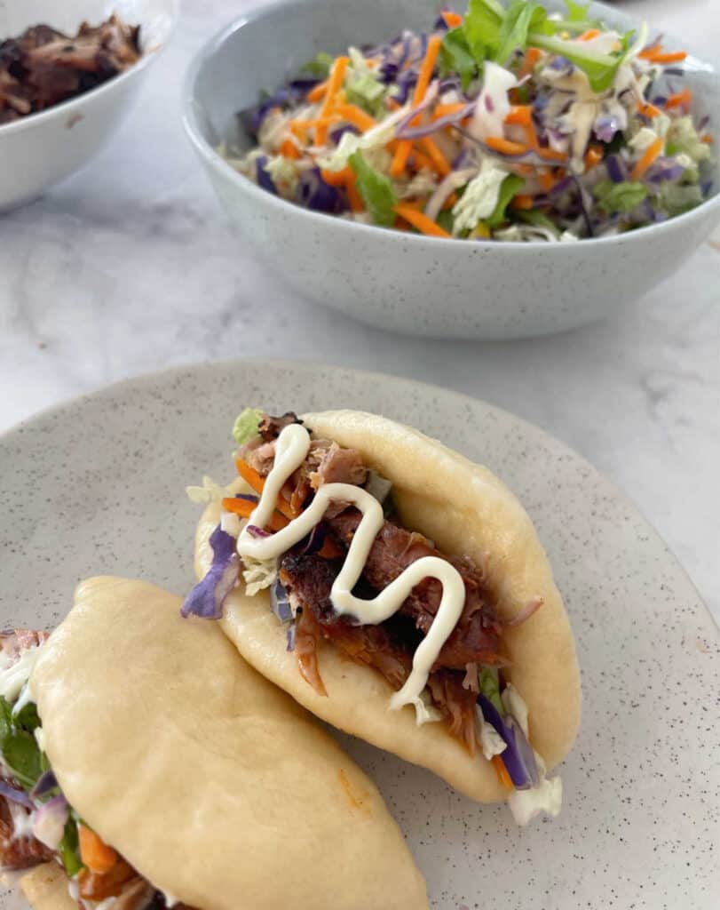 Thermomix Bao Buns filled with salad and roast bbq pork on a speckled plate.