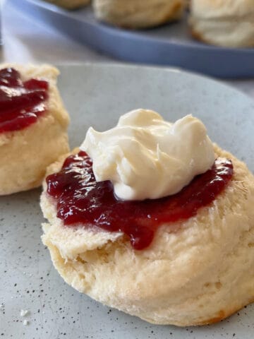 Scones on a green speckle plate with jam and cream.