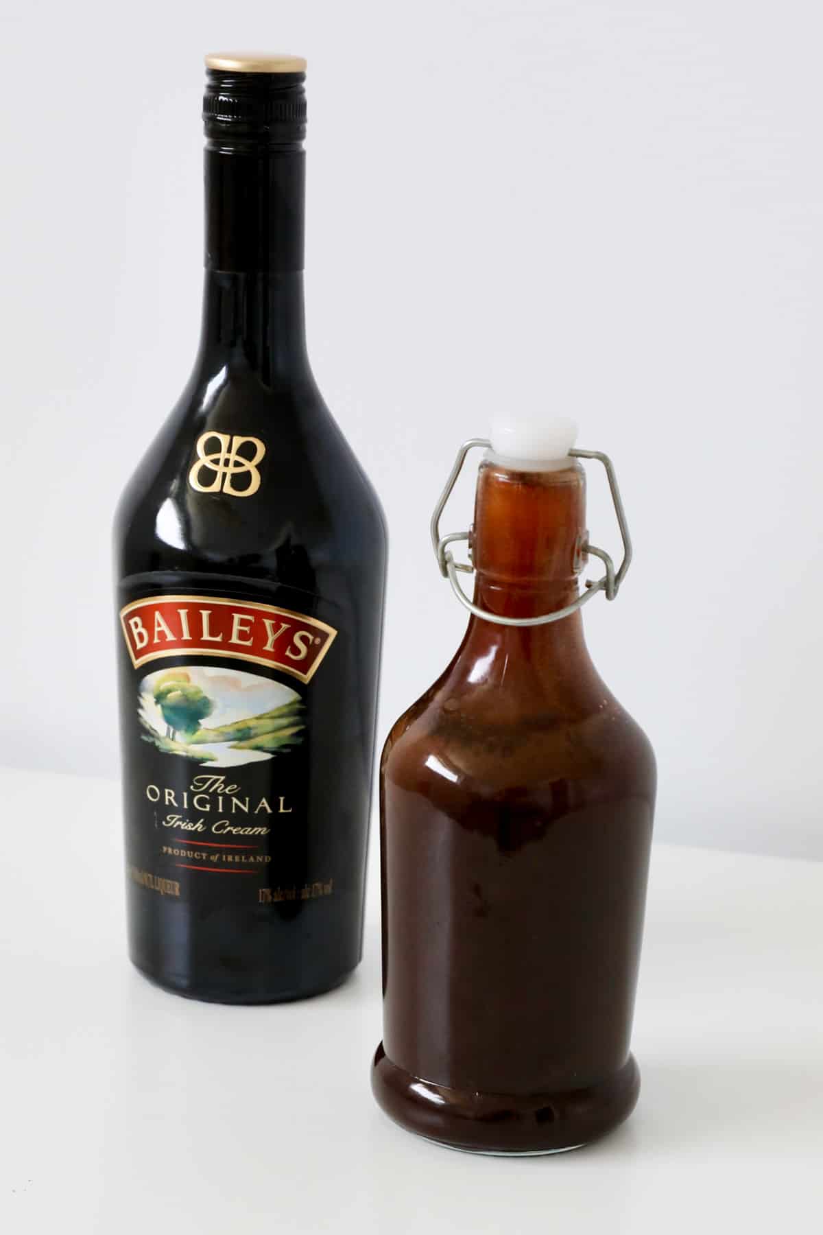 A glass of homemade chocolate sauce in front of a bottle of Baileys Irish cream.
