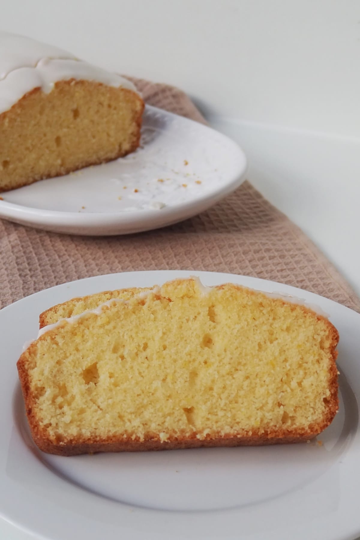 Two slices of Orange butter cake on a white plate. in the background is the rest of the cake on a white serving platter.