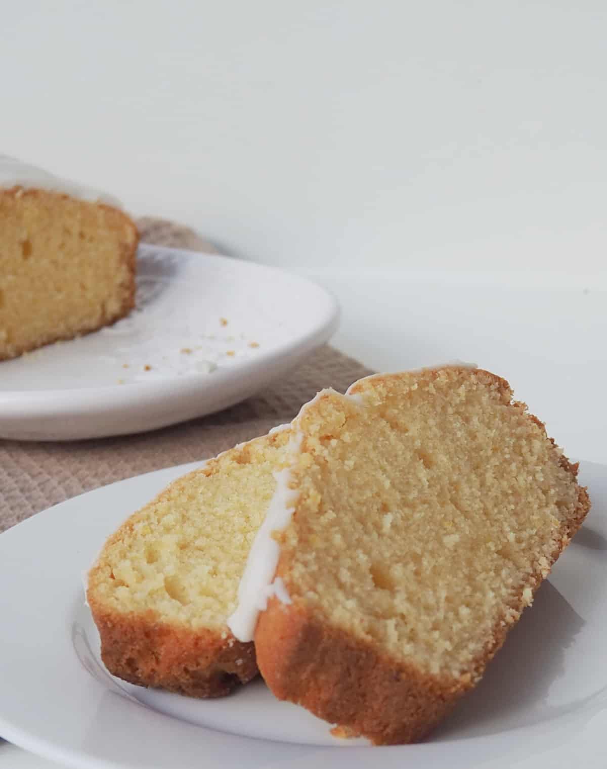 Side view of Two slices of Orange butter cake on a white plate. in the background is the rest of the cake on a white serving platter.