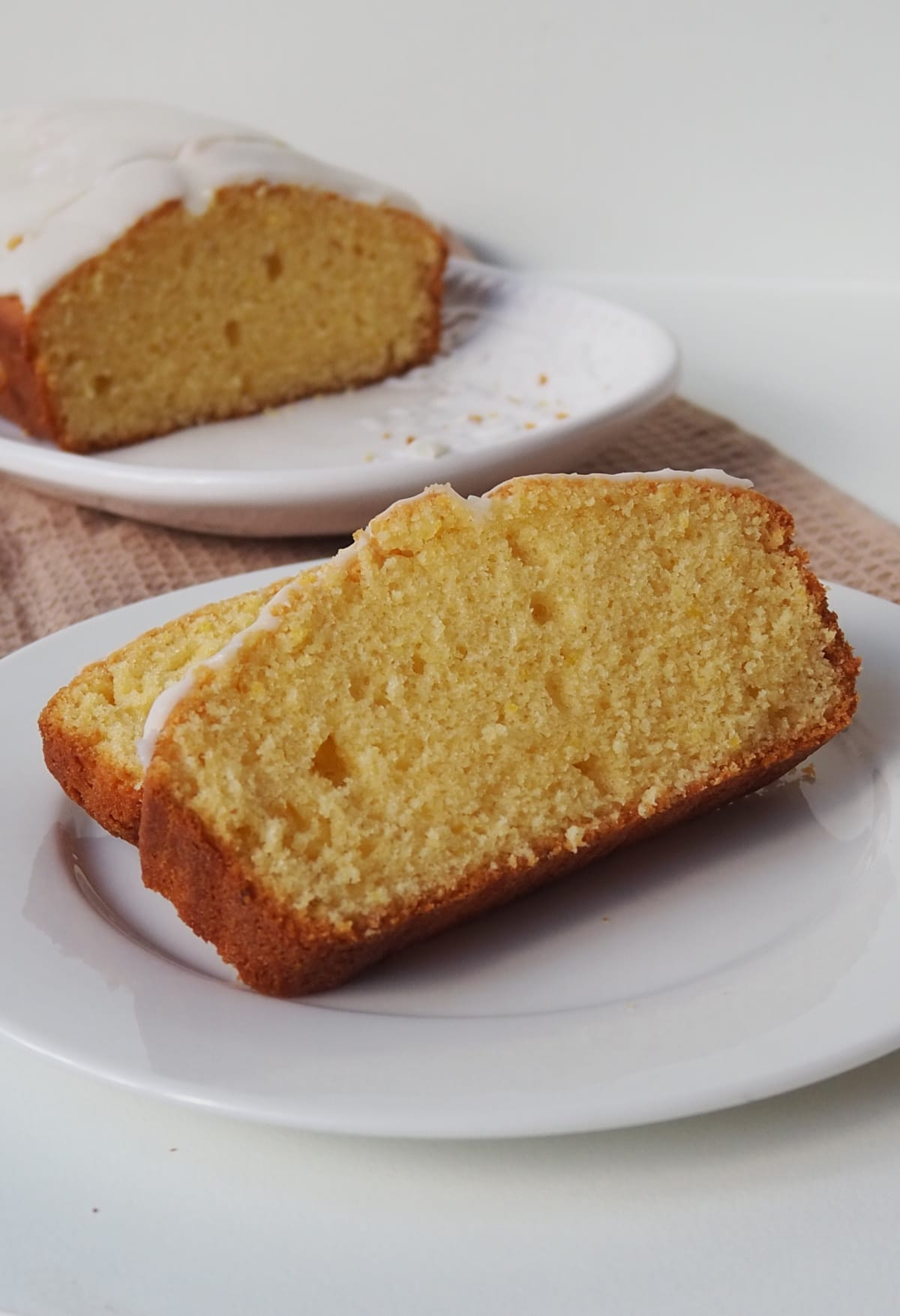 Front side view of Two slices of Orange butter cake on a white plate. in the background is the rest of the cake on a white serving platter.
