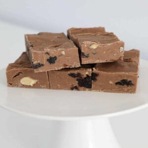 Chocolate fudge with almonds and raisins on a white cake stand.