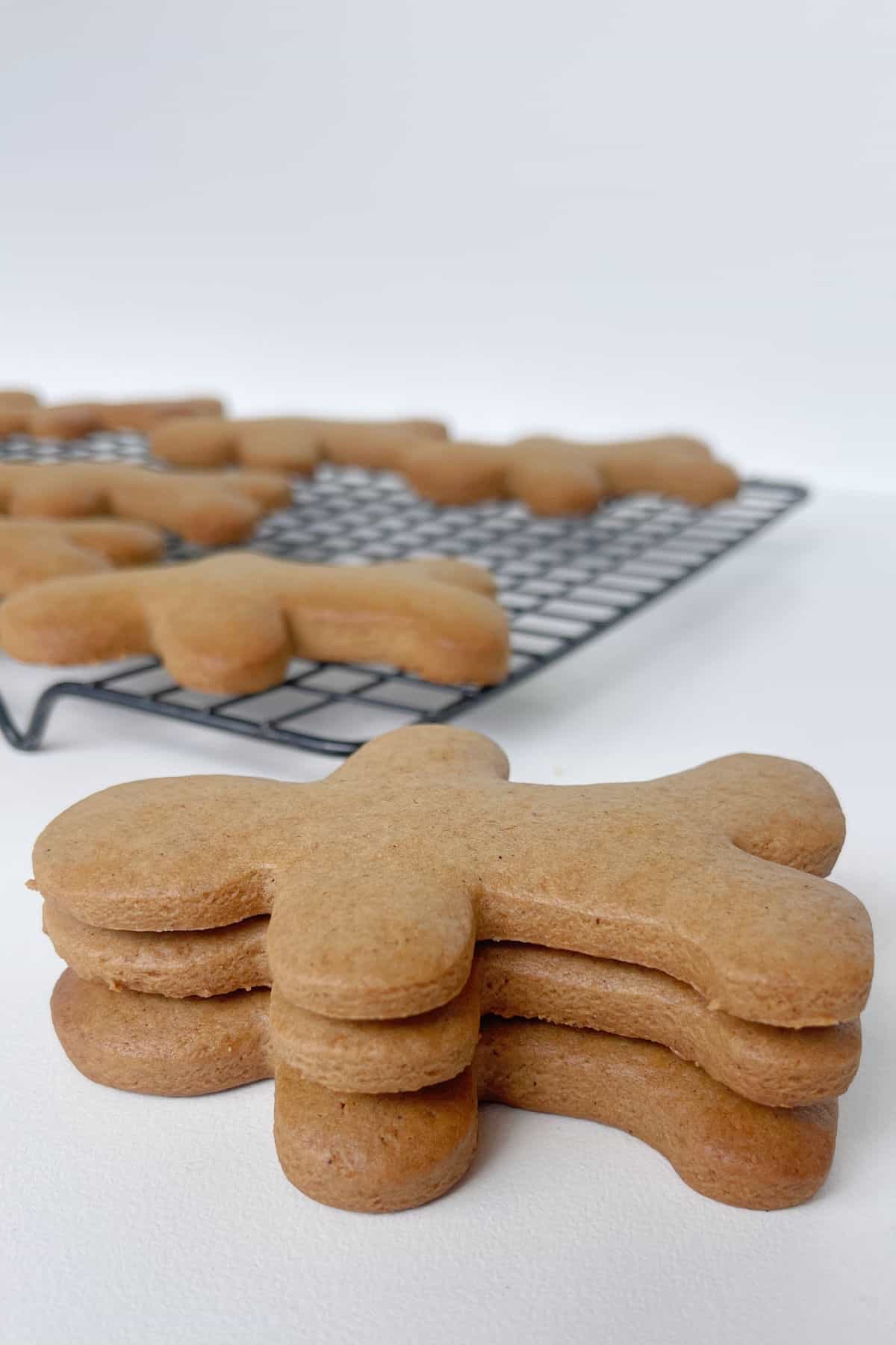 Three gingerbread people stacked on top of each other. In the background is a wire rack with more biscuits.