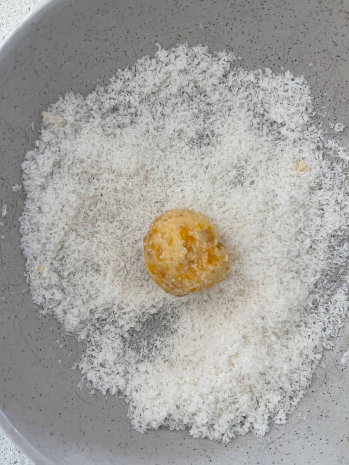 mixture in a bowl of coconut ready to be rolled.