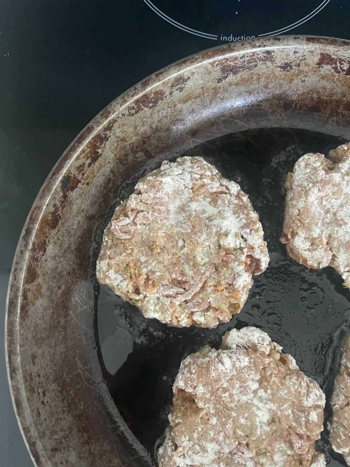 rissole patties cooking in a frying pan.