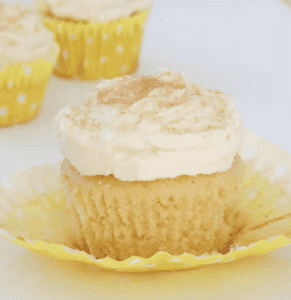 Lemon cupcake with lemon butter creaming icing sitting on white surface with cupcake wrapper pulled down.