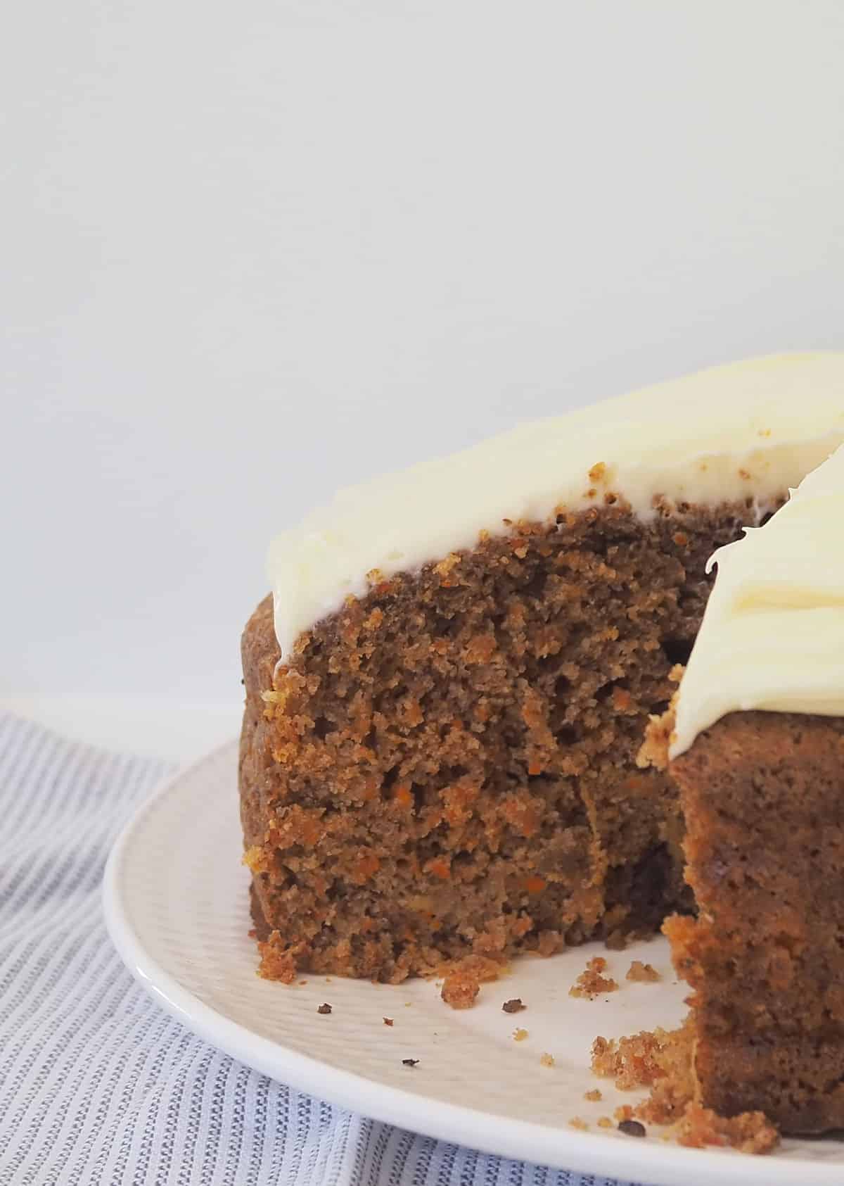 Whole Carrot Cake topped with cream cheese frosting with a pice removed, sitting on a white plate.